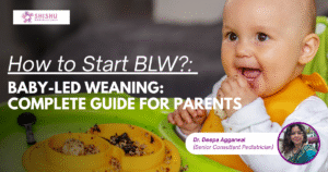 A smiling baby sitting in a high chair self-feeding soft vegetables and fruits — representing independence, exploration, and baby-led weaning during family mealtime. baby-led weaning India, BLW guide for parents, baby self-feeding, pediatrician advice India, how to start BLW, Dr. Deepa Aggarwal pediatrician, baby nutrition India, baby eating solids, working mom feeding tips, healthy baby meals, baby feeding development, baby led weaning India, self feeding baby, BLW guide, pediatric advice for parents, baby starting solids, independent feeding baby, healthy baby diet, family mealtime, baby feeding development
